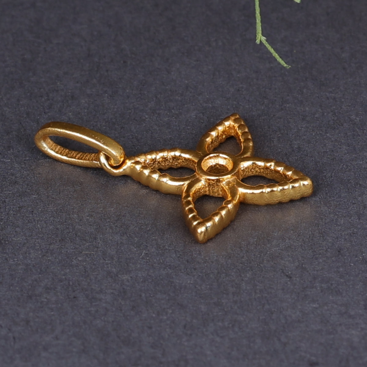 Close up of a textured gold plated four petal flower pendant charm with a central round opening